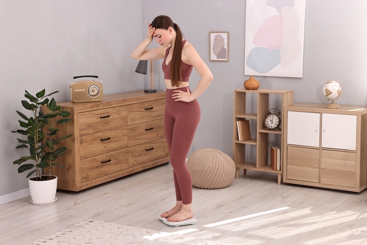Woman in workout clothes standing on scale frustrated by weight loss resistance despite diet and exercise