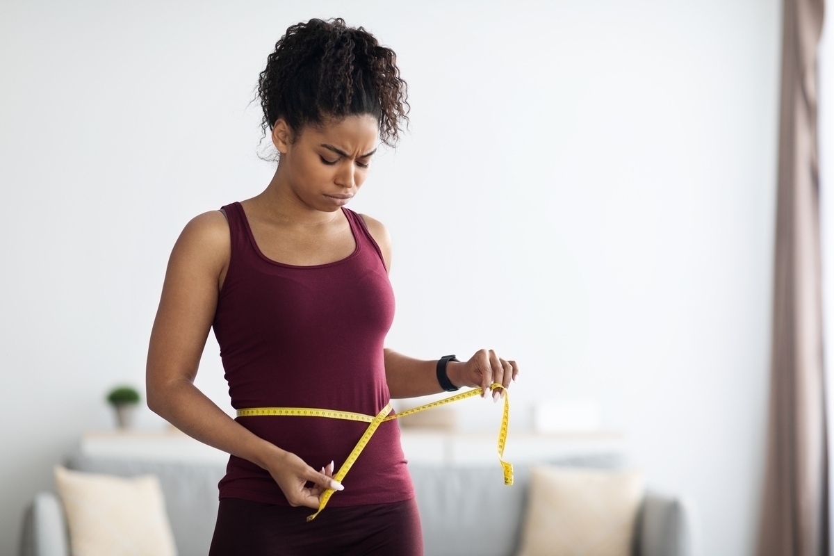 Woman in workout clothes measuring waist frustrated by insulin resistance and weight loss difficulty