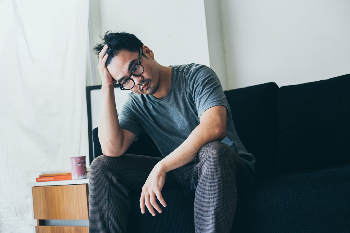 Man sitting on couch with hand to head representing low testosterone and depression mood symptoms