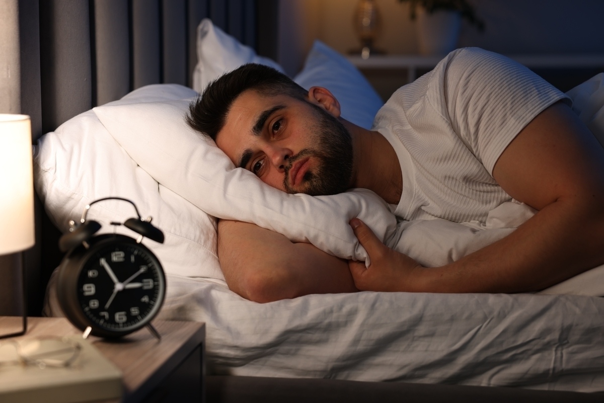 Man lying awake in bed at night with alarm clock representing low testosterone and sleep disruption